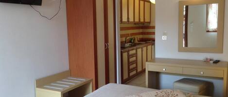 Un dormitorio con una cama, una mesita de noche, un espejo y un televisor montado en la pared.