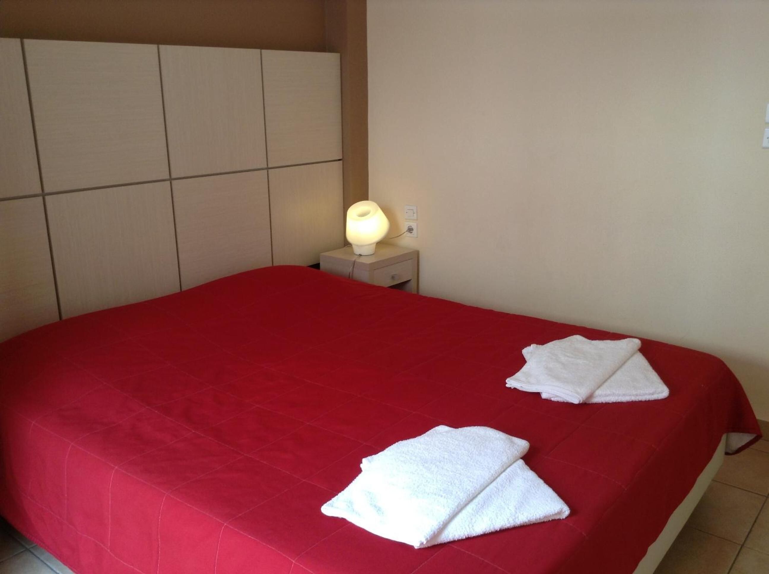 A hotel room with a red bedspread, a bedside lamp, and two white towels on the bed.