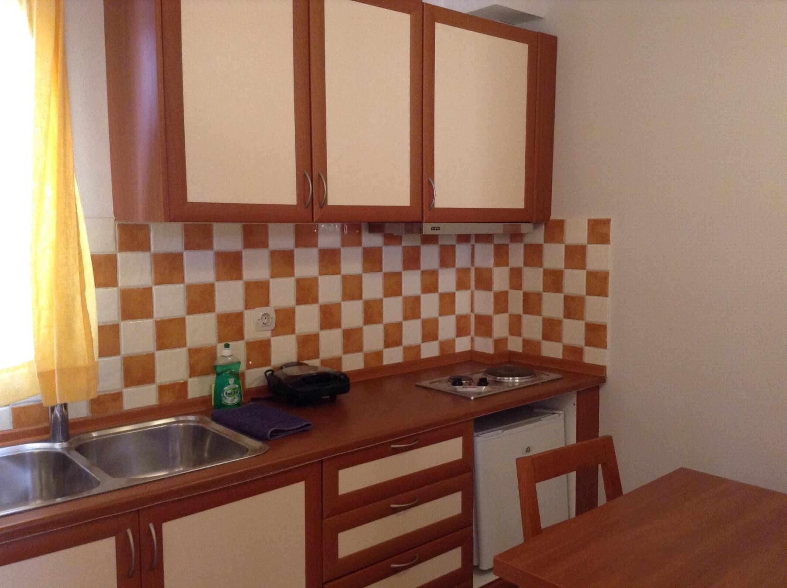 A compact kitchen with wooden cabinets, a checkered backsplash, a sink, a stove, and a refrigerator.