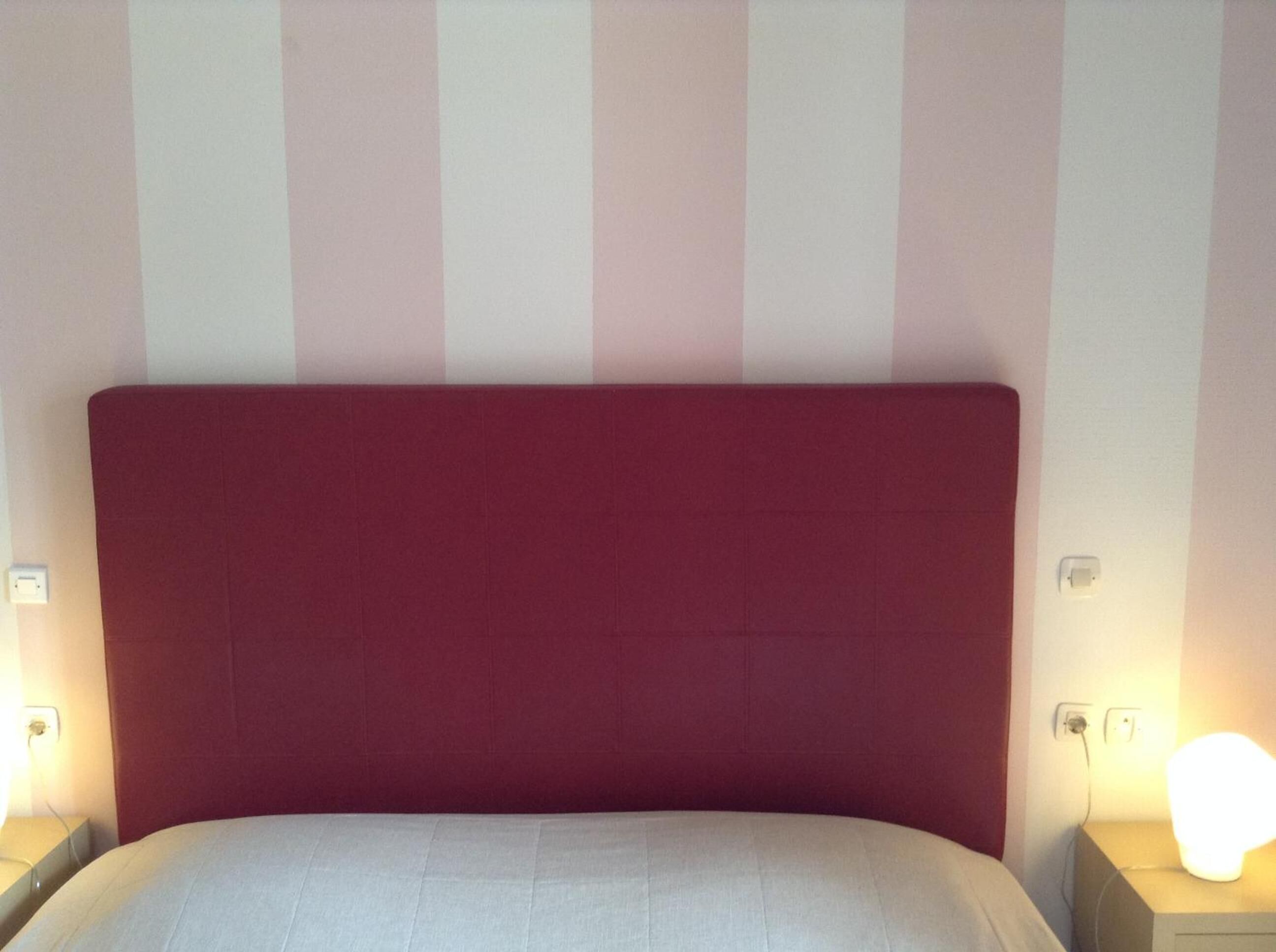 A bed with a red headboard, a bedside lamp, and a wall with vertical stripes.