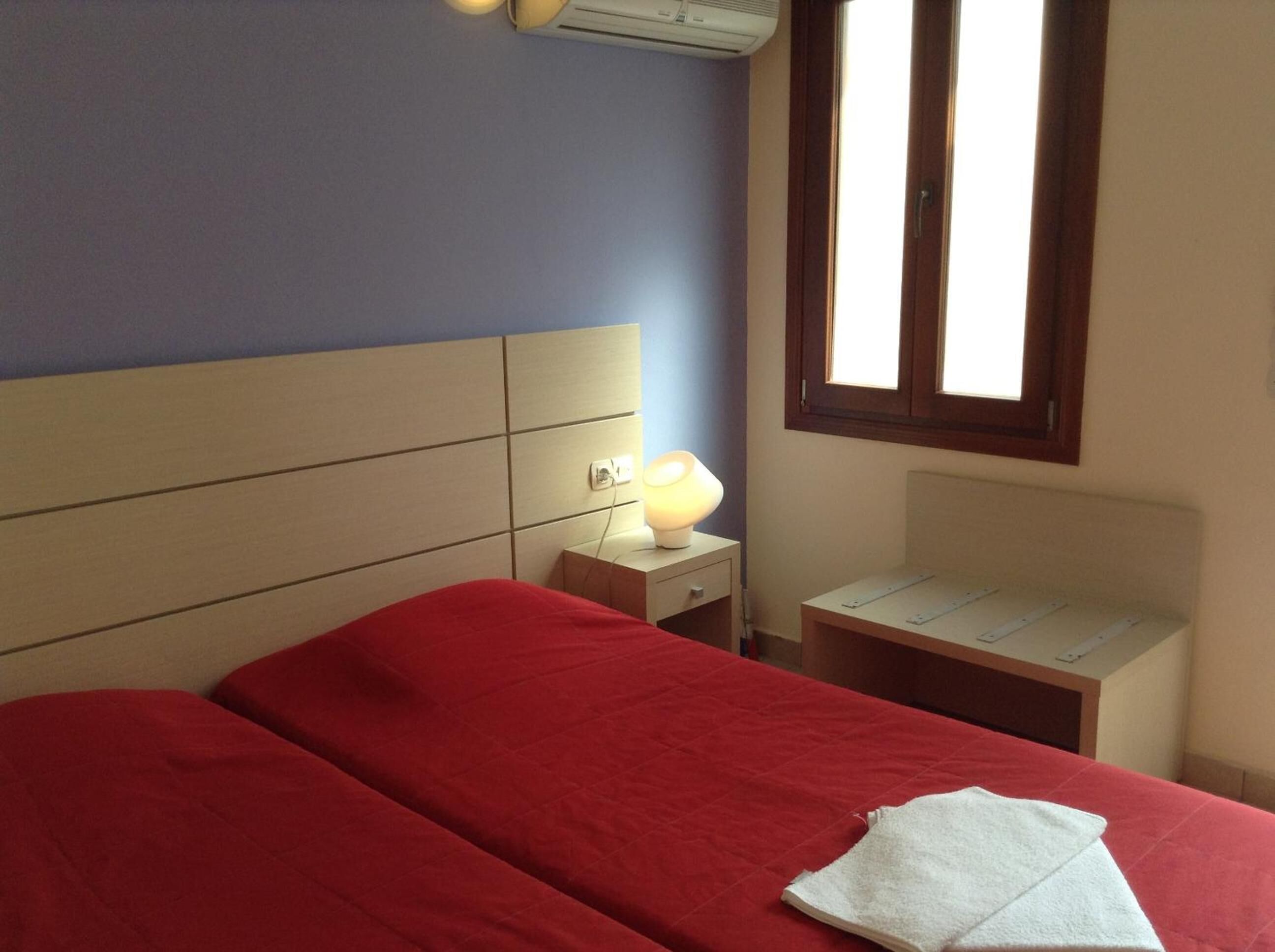 A hotel room with a bed, a nightstand, a lamp, and a window.