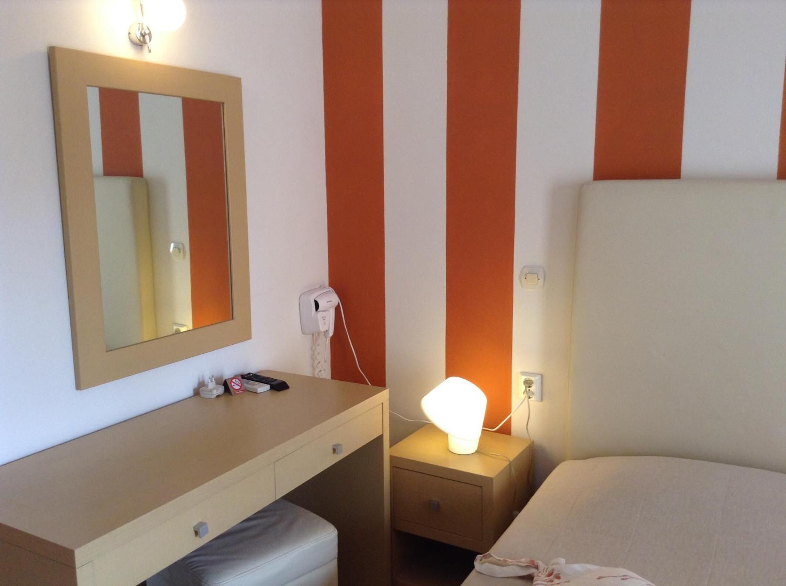 A hotel room with a bed, a bedside table with a lamp, a mirror, and a telephone.