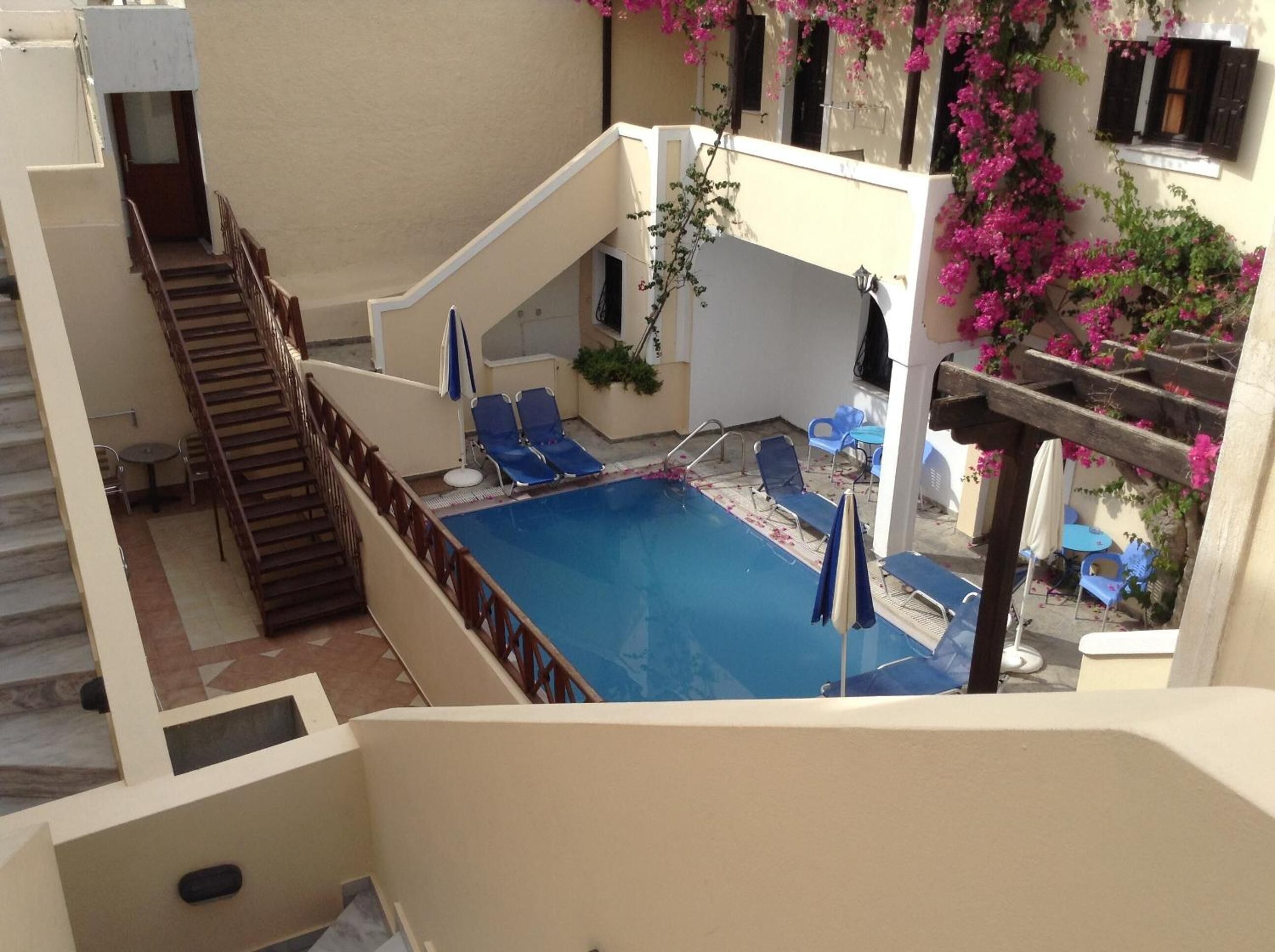 Ein Pool auf dem Dach mit blauen Liegestühlen, einer Treppe und einer Pergola mit rosa Blüten.