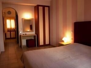 A hotel room with a bed, a desk, a mirror, and a wardrobe. - Antonia Apartments (Santorini)