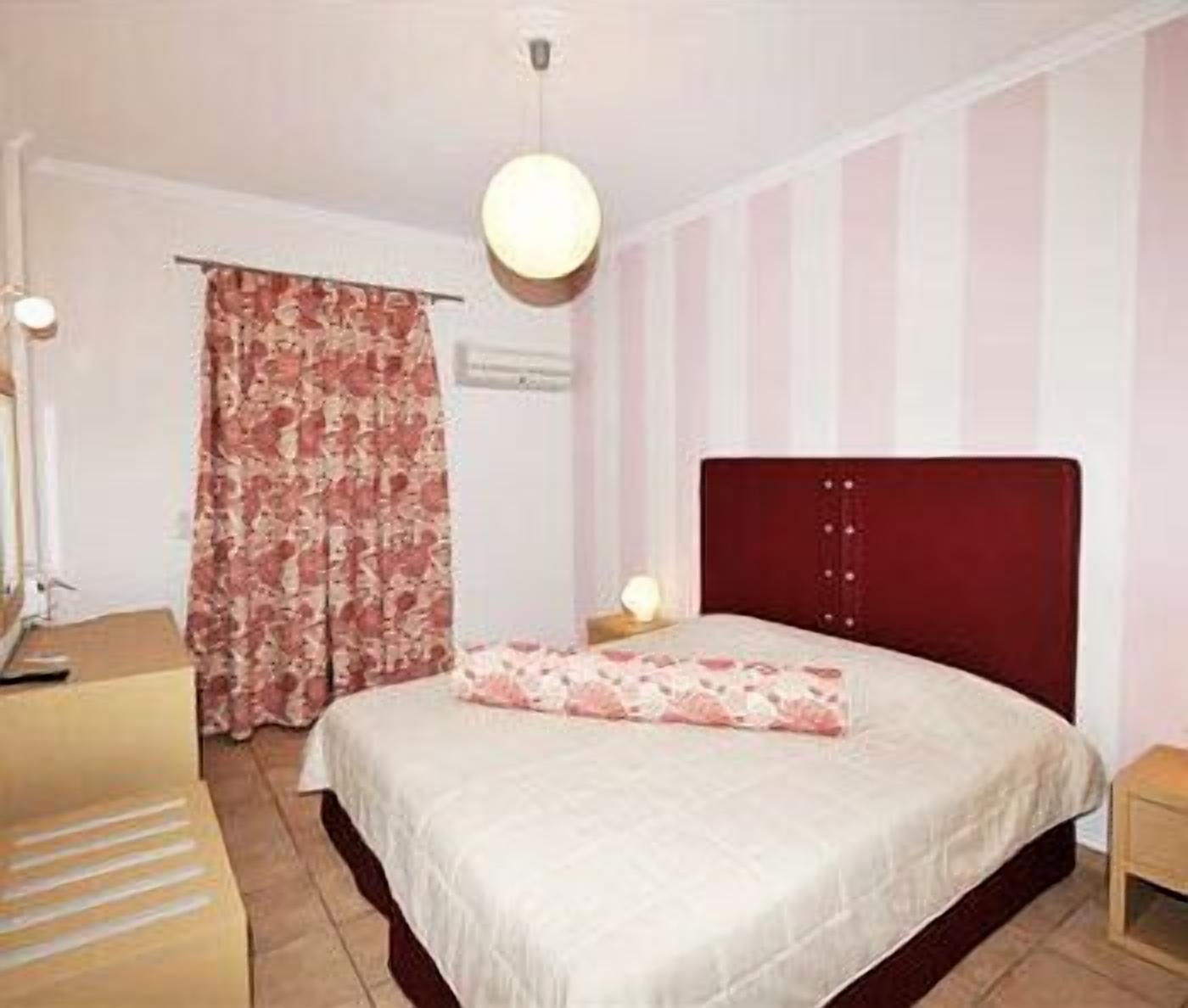 A bedroom with a bed, a nightstand, a lamp, and a window with curtains.