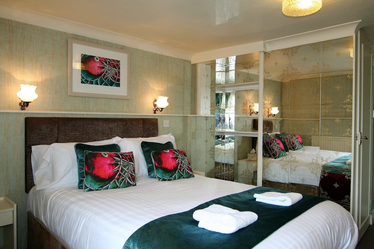 A hotel room with a large bed, two bedside lamps, a framed artwork above the bed, and a mirror with decorative panels.