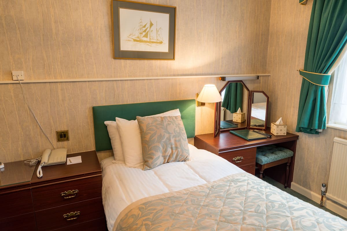 A neatly arranged hotel room with a bed, bedside table, lamp, and a mirror.
