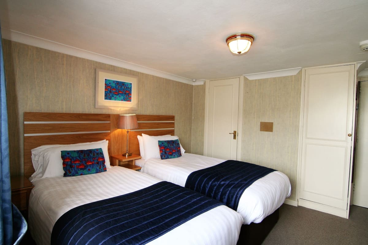 A hotel room with two beds, a nightstand, a lamp, a framed picture on the wall, and a door.