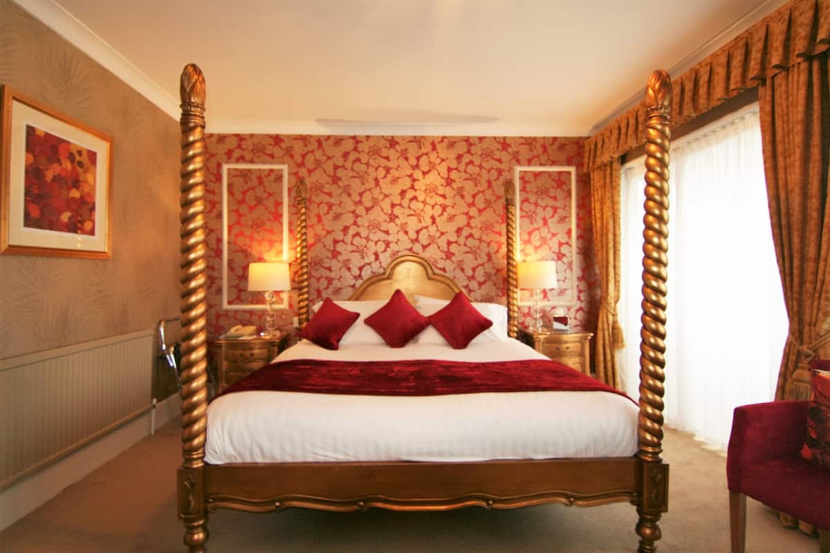 A four-poster bed with a wooden frame and red bedding, flanked by two nightstands with lamps, in a room with floral wallpaper and a red accent wall.