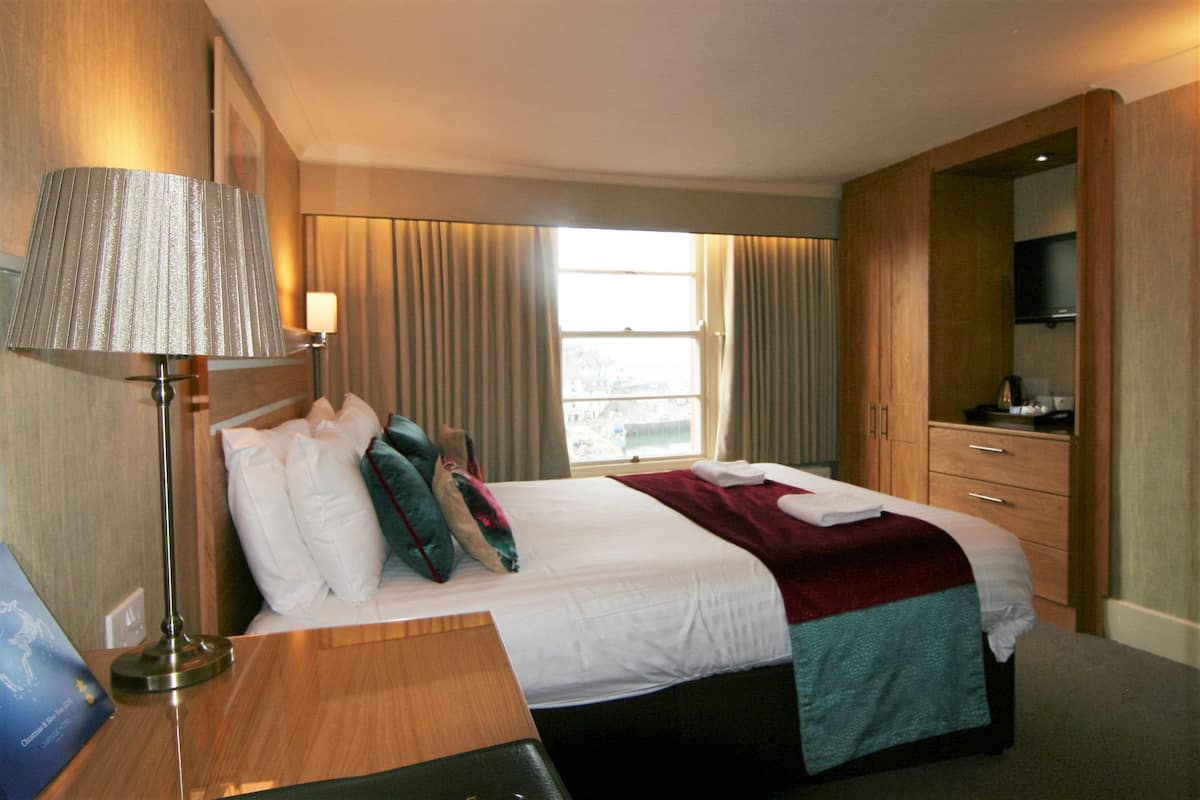 A hotel room with a bed, a desk, a lamp, a TV, and a window with curtains.