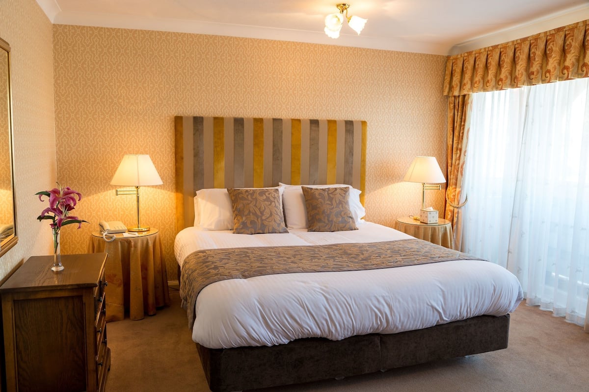 A hotel room with a large bed, two bedside tables with lamps, a mirror, and a window with curtains.