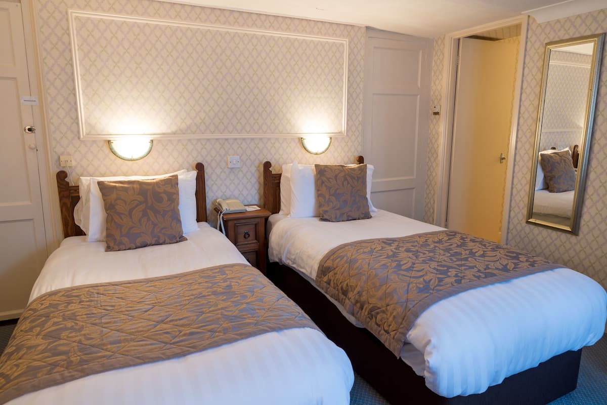 A hotel room with two beds, each with a headboard, bedside tables, lamps, and a mirror.