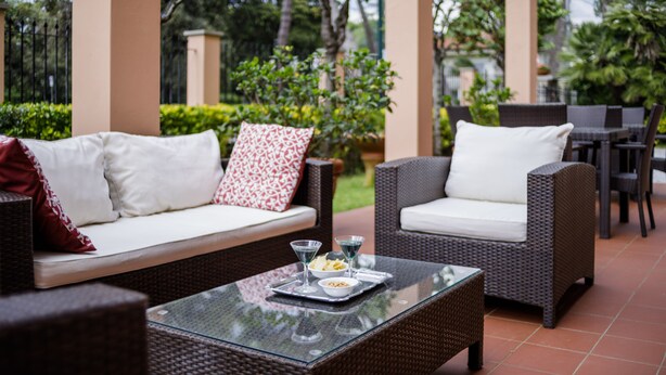 An outdoor patio area with wicker furniture, including a sofa and chairs, and a glass table with a tray of food and drinks. - Hotel Astor Victoria (Forte dei Marmi)