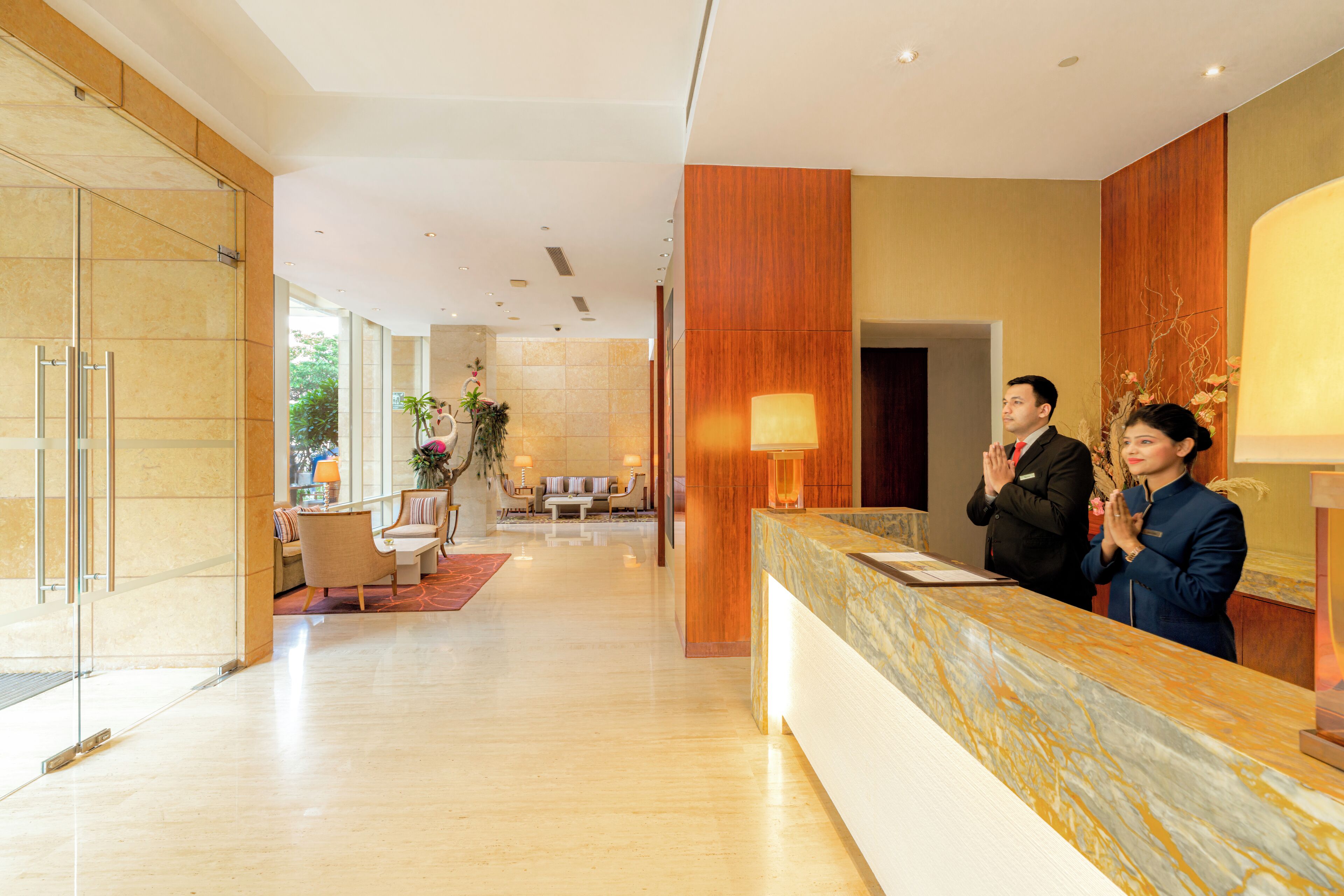 Un hall d’accueil d’hôtel avec un comptoir en marbre, un espace salon à l’arrière-plan et une entrée avec une porte en verre.