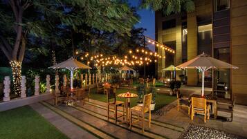 An outdoor patio area with string lights, wooden tables and chairs, and umbrellas.