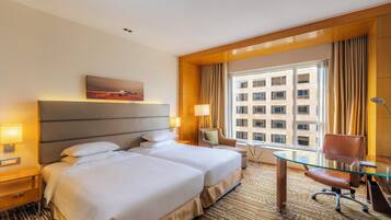 A hotel room with two beds, a desk, a chair, a window with curtains, and a painting on the wall.