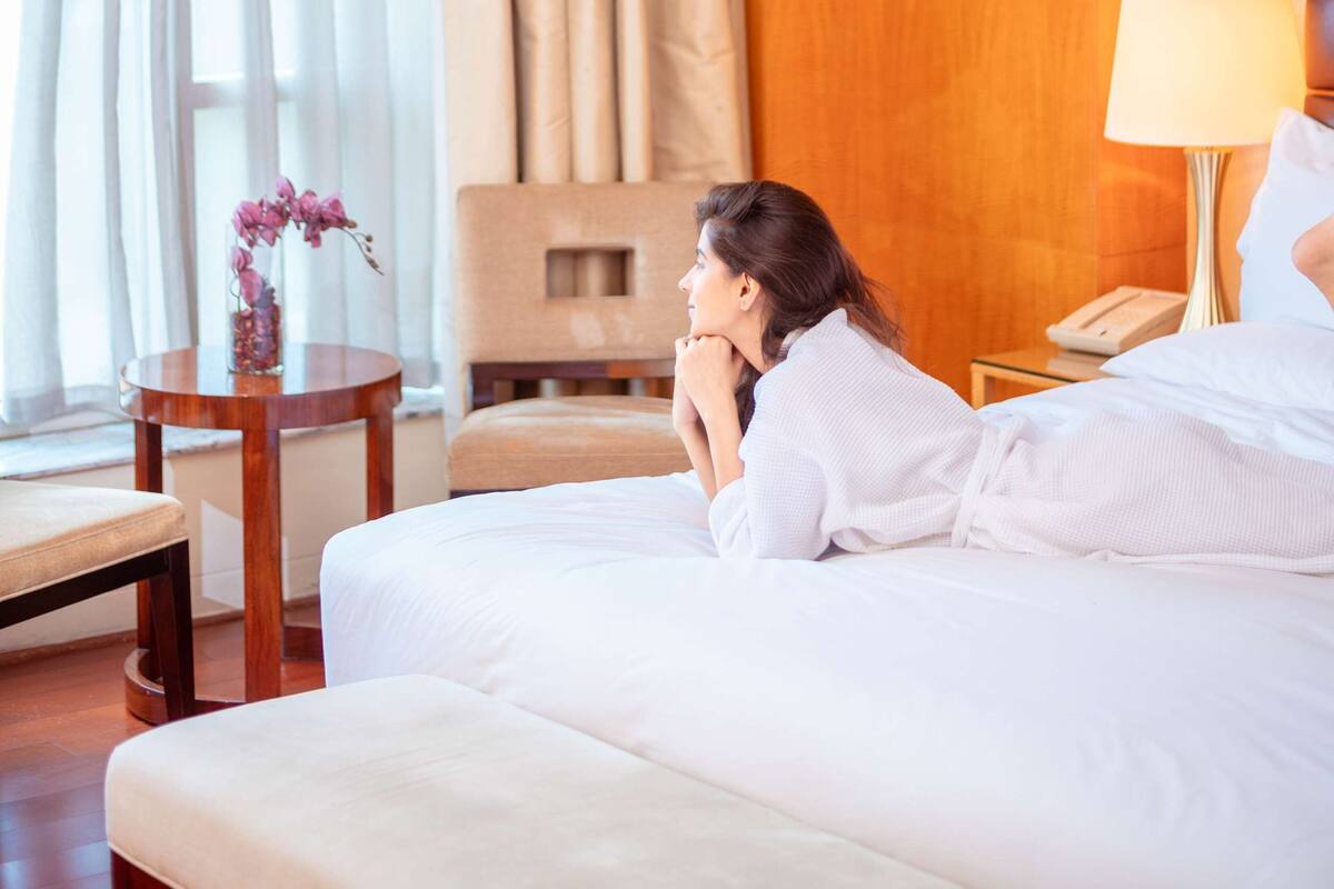 A hotel room with a bed, a bedside table with a lamp, a chair, and a window with curtains.