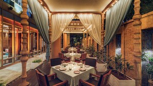 An indoor dining area with tables set for a meal, surrounded by wooden chairs and draped curtains.