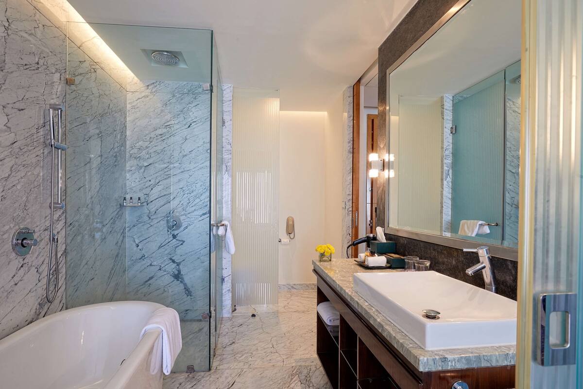 A modern bathroom with a glass-enclosed shower, a freestanding bathtub, and a large mirror with lights.