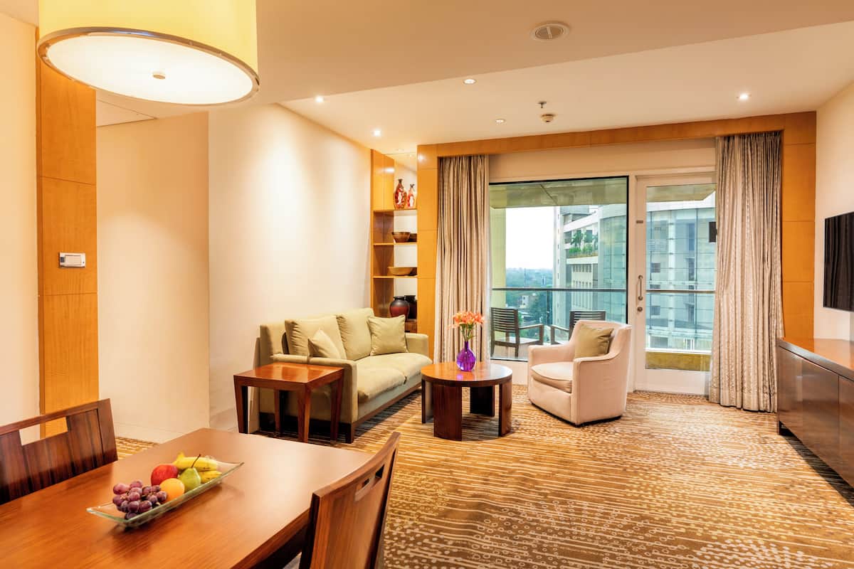 A modern hotel room with a dining area, a sofa, a chair, and a balcony with curtains.