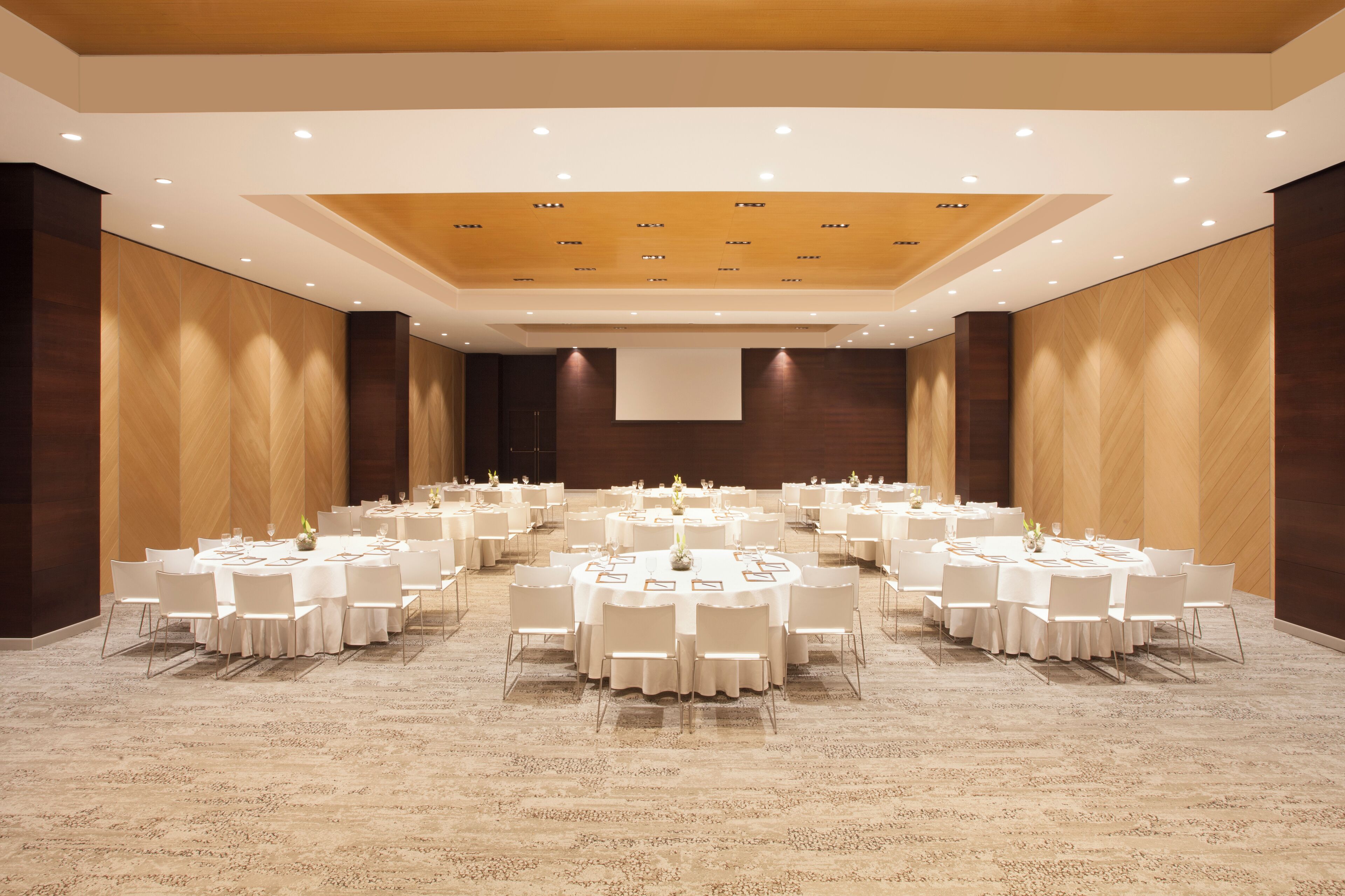A large conference room with multiple round tables and white chairs, arranged in a symmetrical layout.