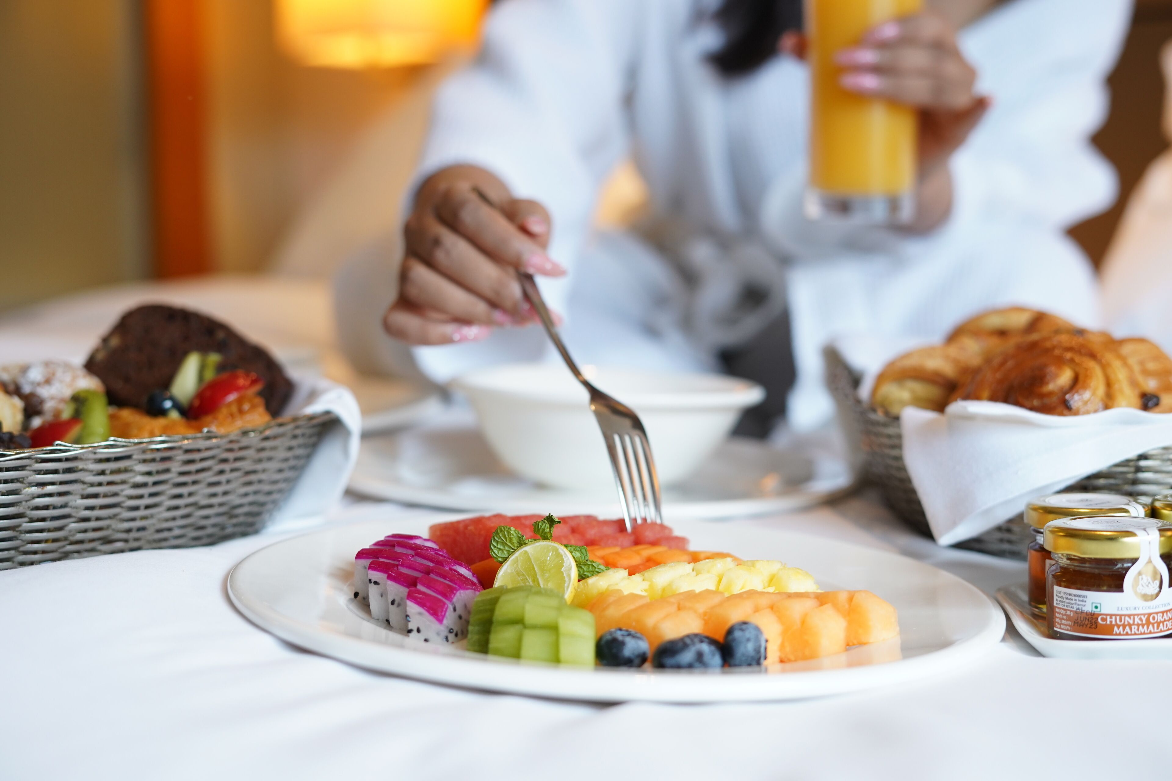 A breakfast setting with a plate of fruit, croissants, and a glass of orange juice.