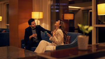 A couple sitting on a blue sofa in a well-lit room with lamps and a window.
