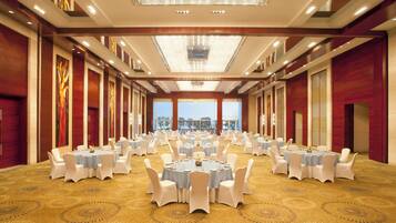 A large banquet hall with round tables, white chairs, and a patterned carpet.