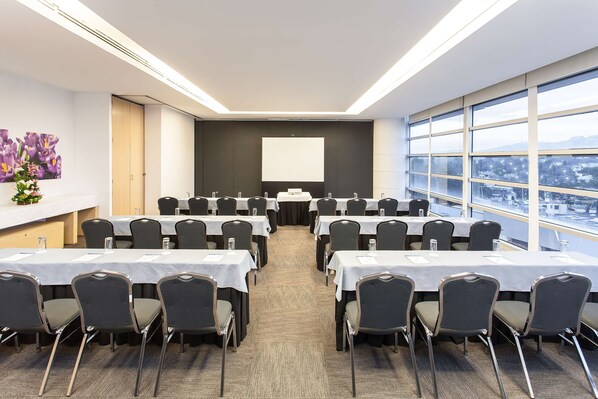 Ein Konferenzraum mit Tischen, Stühlen, einer Projektionsleinwand und großen Fenstern mit Blick auf die Stadt.
