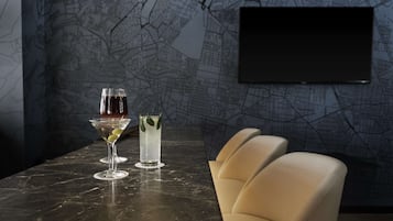 A bar area with two glasses of wine and a cocktail, a flat-screen TV mounted on the wall, and a marble countertop.