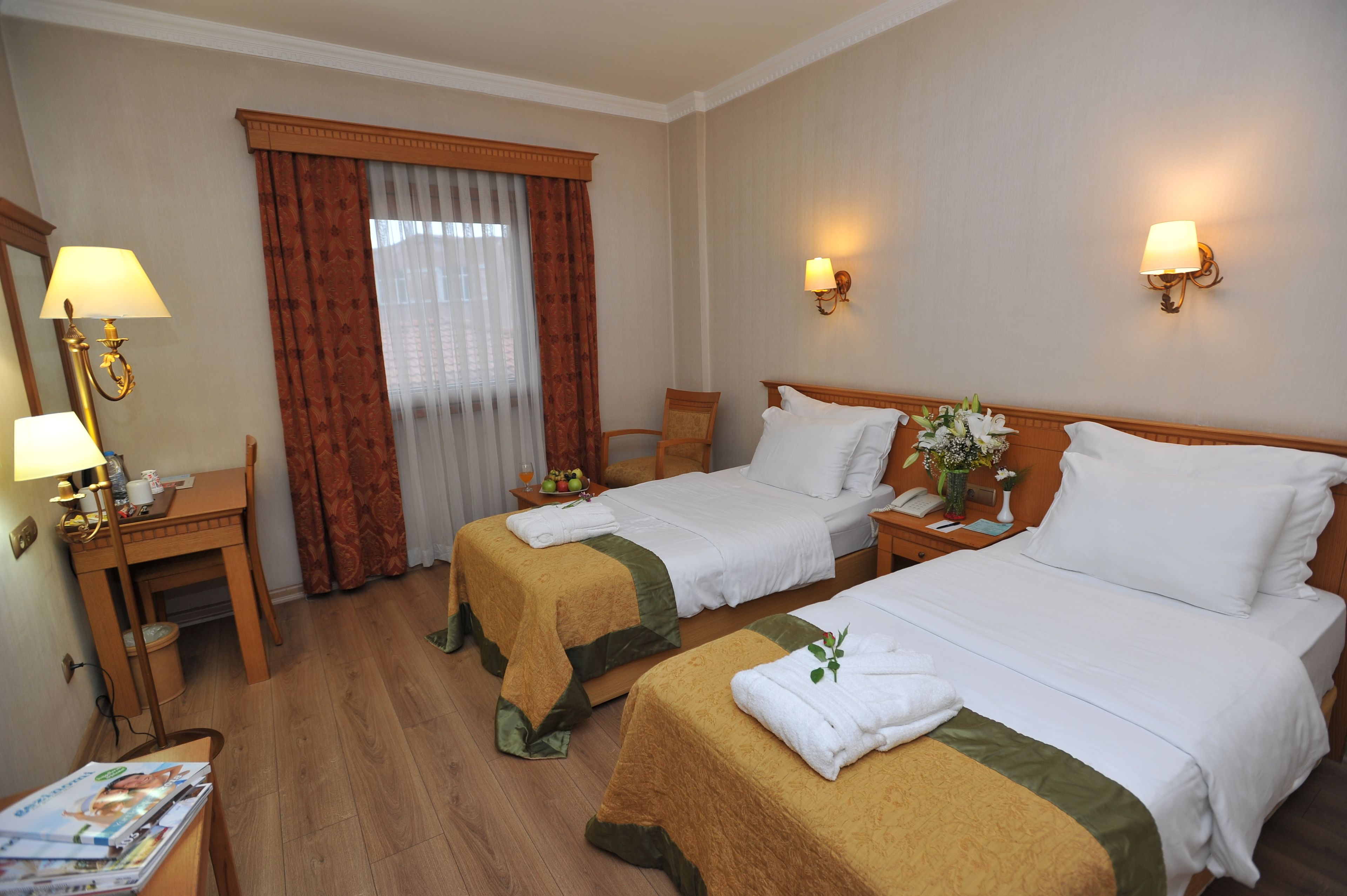 Habitación de hotel con dos camas, un escritorio con lámpara, una silla y una ventana con cortinas.