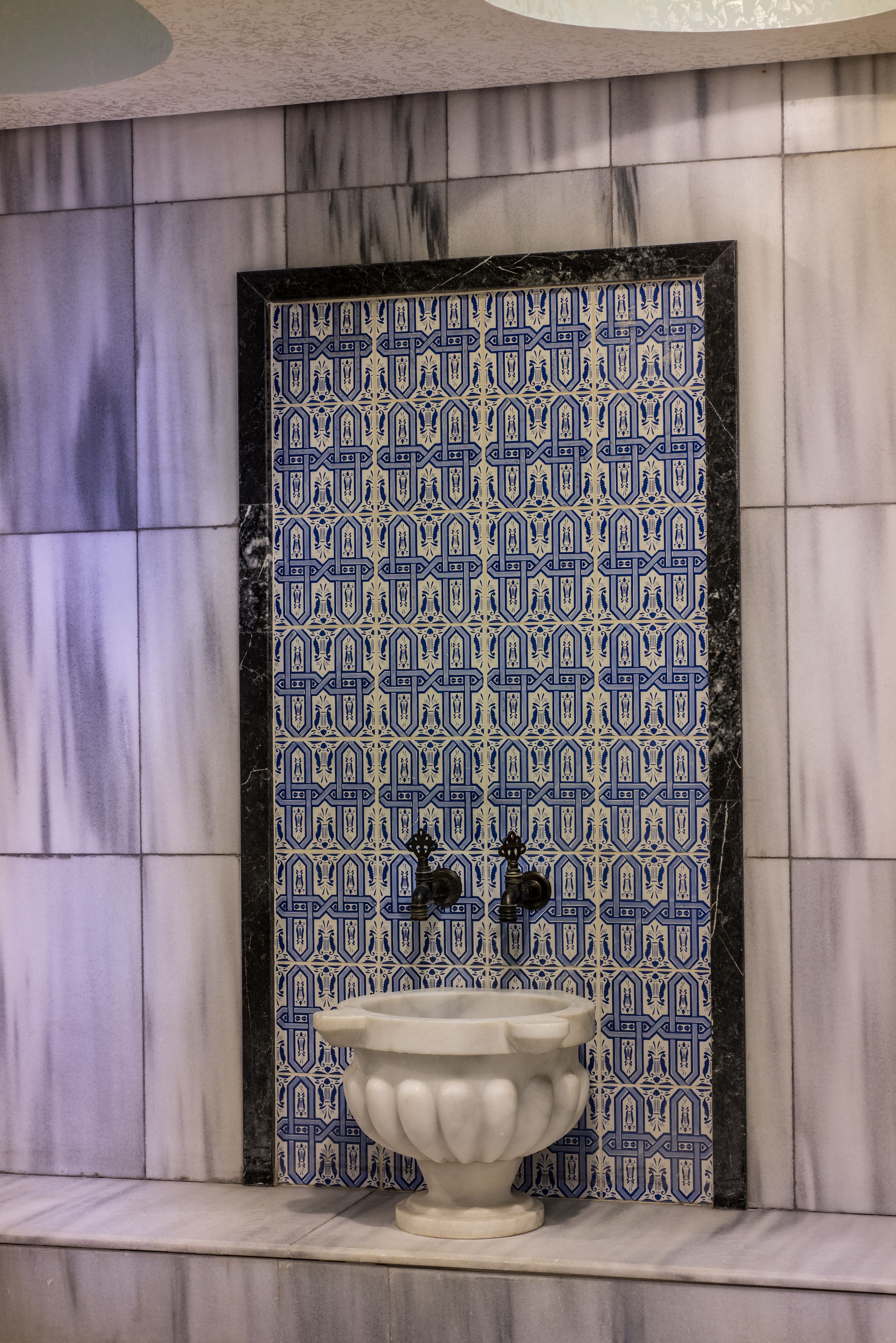 A bathroom with a patterned tile wall, a marble floor, and a white pedestal sink.