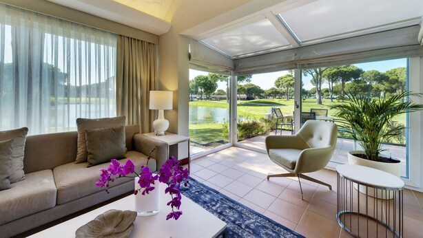 A modern living room with a sofa, armchair, and a view of a golf course through large windows. - ROBINSON NOBILIS - All Inclusive (Serik)