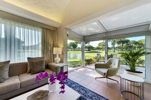 A modern living room with a sofa, armchair, and a view of a golf course through large windows.