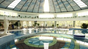A large indoor swimming pool with a dome ceiling, seating areas, and a statue. - ROBINSON NOBILIS - All Inclusive (Serik)