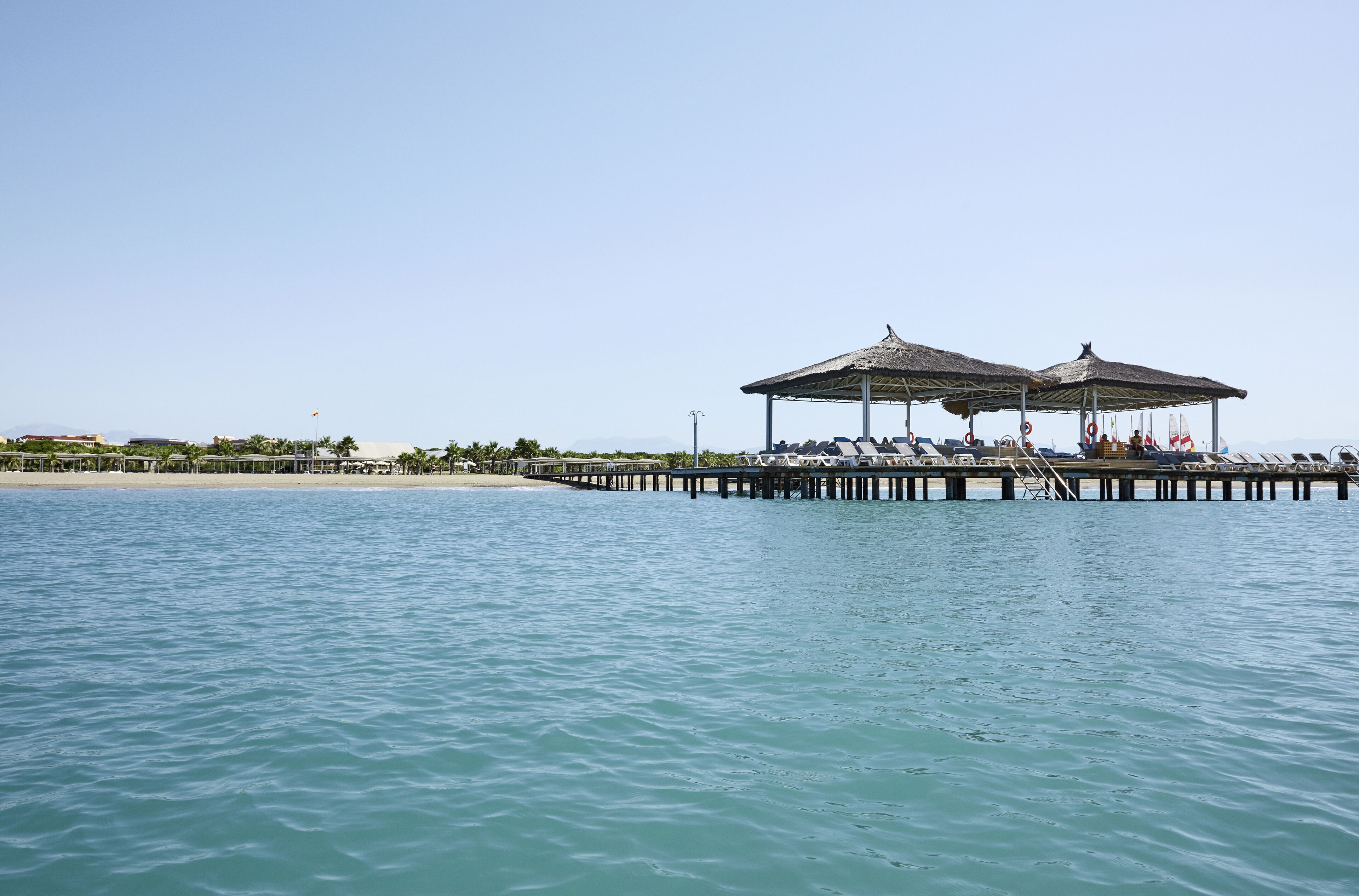 Un muelle con dos zonas a la sombra y sillones de descanso que se adentran en el agua.