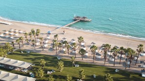 An aerial view of a beach resort with multiple palm trees, beach umbrellas, and a pier extending into the water. - ROBINSON NOBILIS - All Inclusive (Serik)