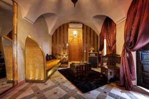 A luxurious room with a large bed, a chest of drawers, a small table, and a decorative lamp.