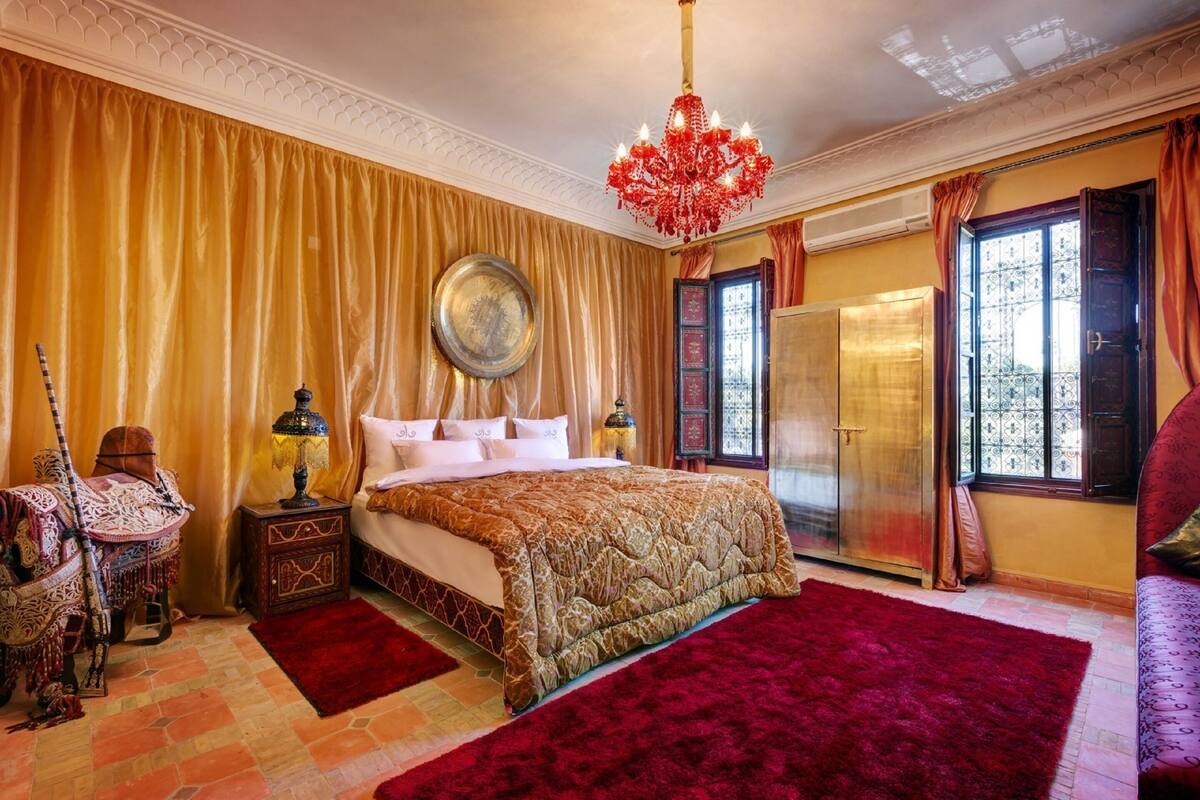 Una habitación con una cama grande, una araña, un armario y una alfombra roja.