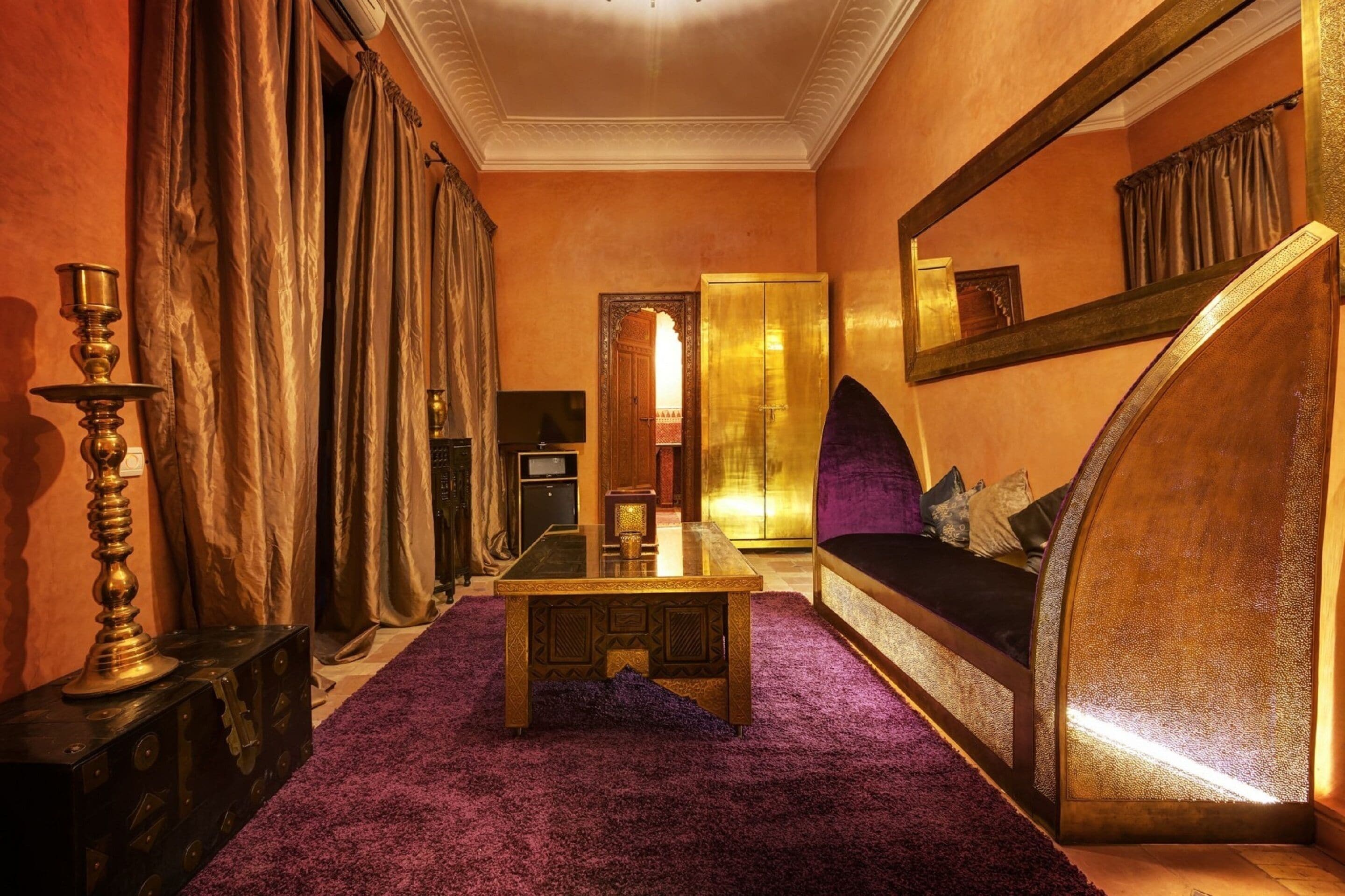 A room with a purple carpet, a wooden coffee table, a sofa with cushions, a large mirror, and a wardrobe.