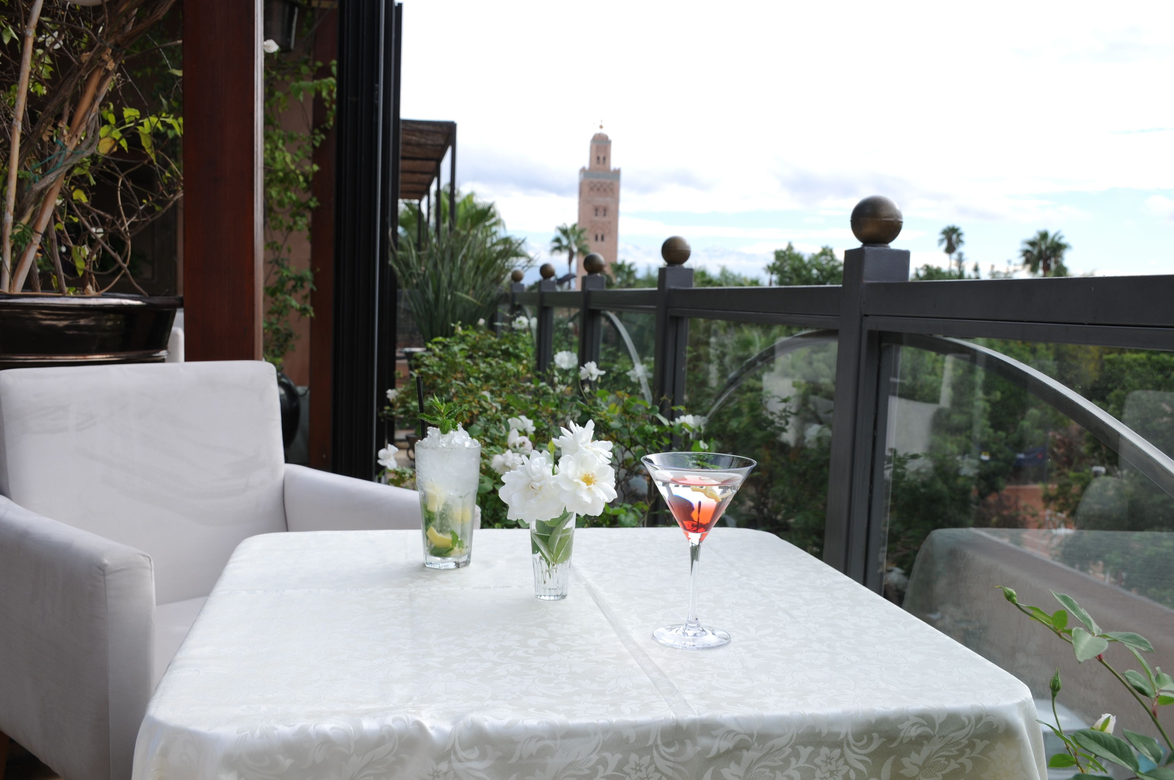 A table with a white tablecloth, two vases with flowers, and a martini glass with a red drink.