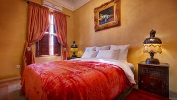 Quarto de hotel com uma cama grande, uma mesa de cabeceira com abajur, um quadro na parede e uma janela com cortinas.