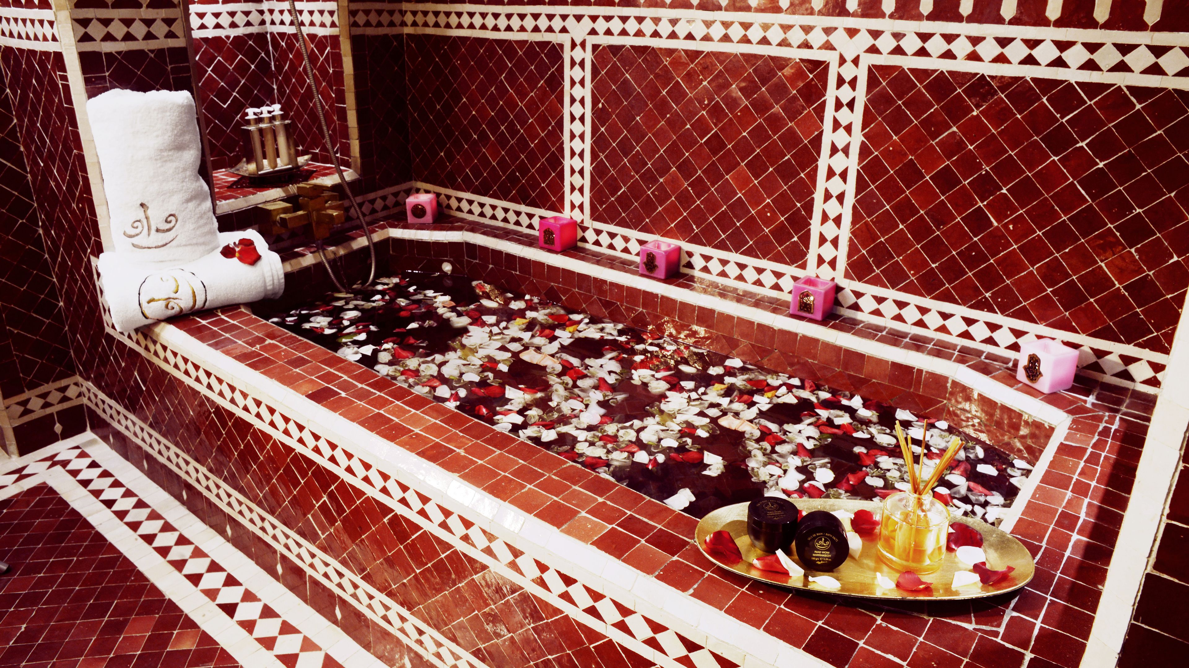 Une salle de bain avec une grande baignoire remplie de pétales de rose, une serviette blanche et divers produits de toilette.