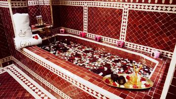 Une salle de bain avec une grande baignoire remplie de pétales de rose, une serviette blanche et divers produits de toilette.