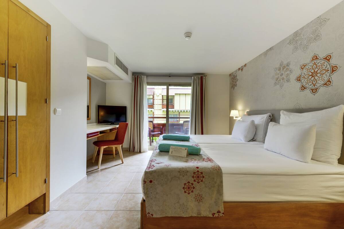A hotel room with a bed, a desk with a chair, a television, and a view of the outside.