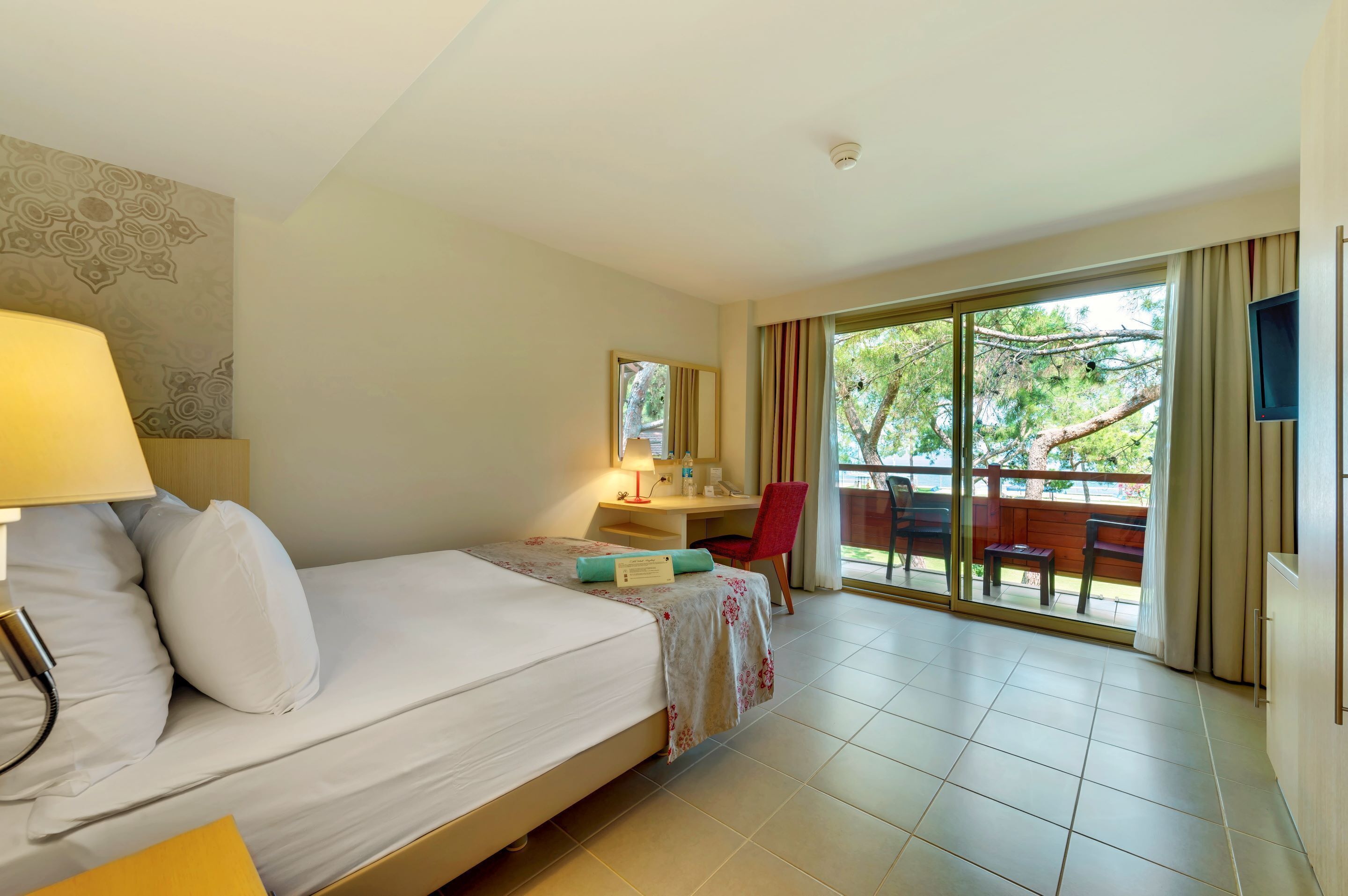A hotel room with a bed, desk, chair, and a view of the outdoors.