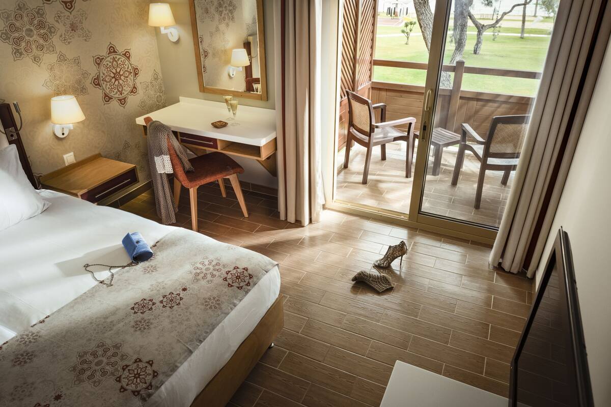 A hotel room with a bed, desk, and a balcony with chairs.