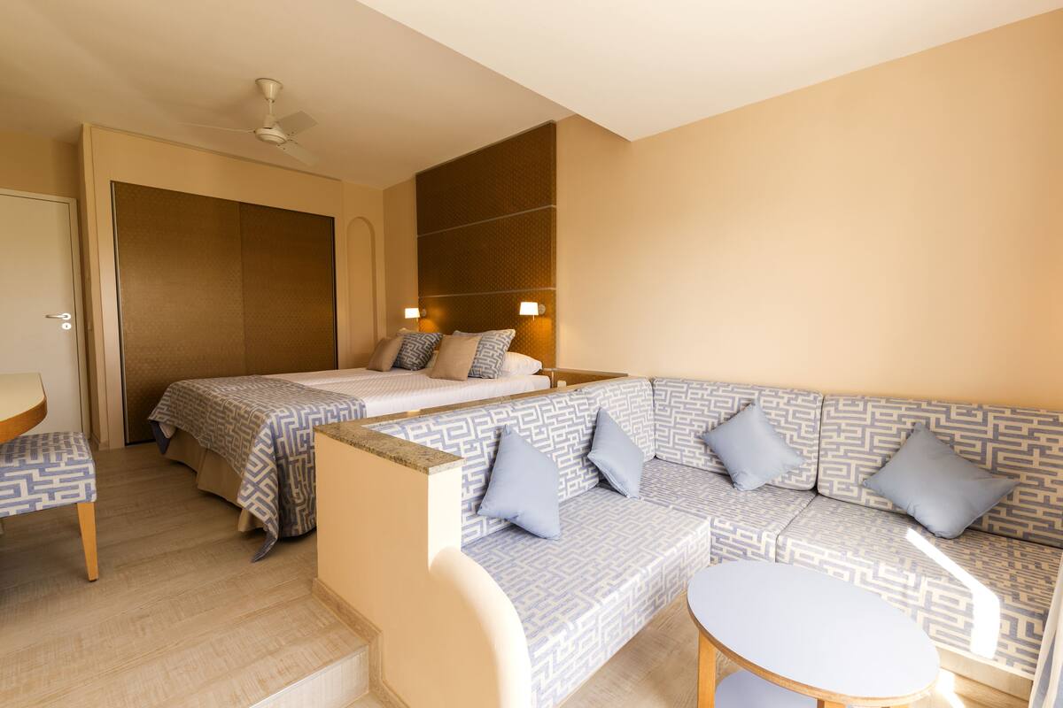 Une chambre d’hôtel avec un lit, un canapé, une petite table et un ventilateur de plafond.