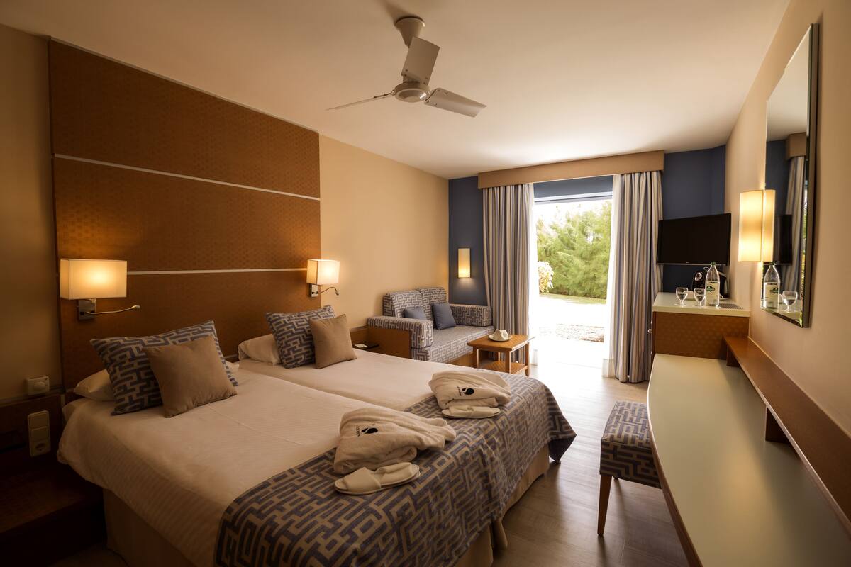 Une chambre d’hôtel avec deux lits, un bureau, une chaise, une télévision et un ventilateur de plafond.