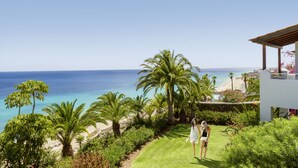 A coastal property with a view of the ocean, palm trees, and a white building with a covered patio.